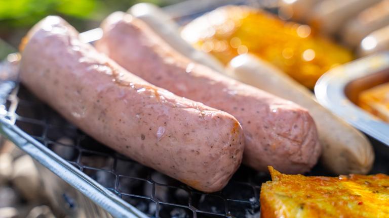 Rohe vegane Würstchen liegen neben Tofu-Stücken auf einem Grill.