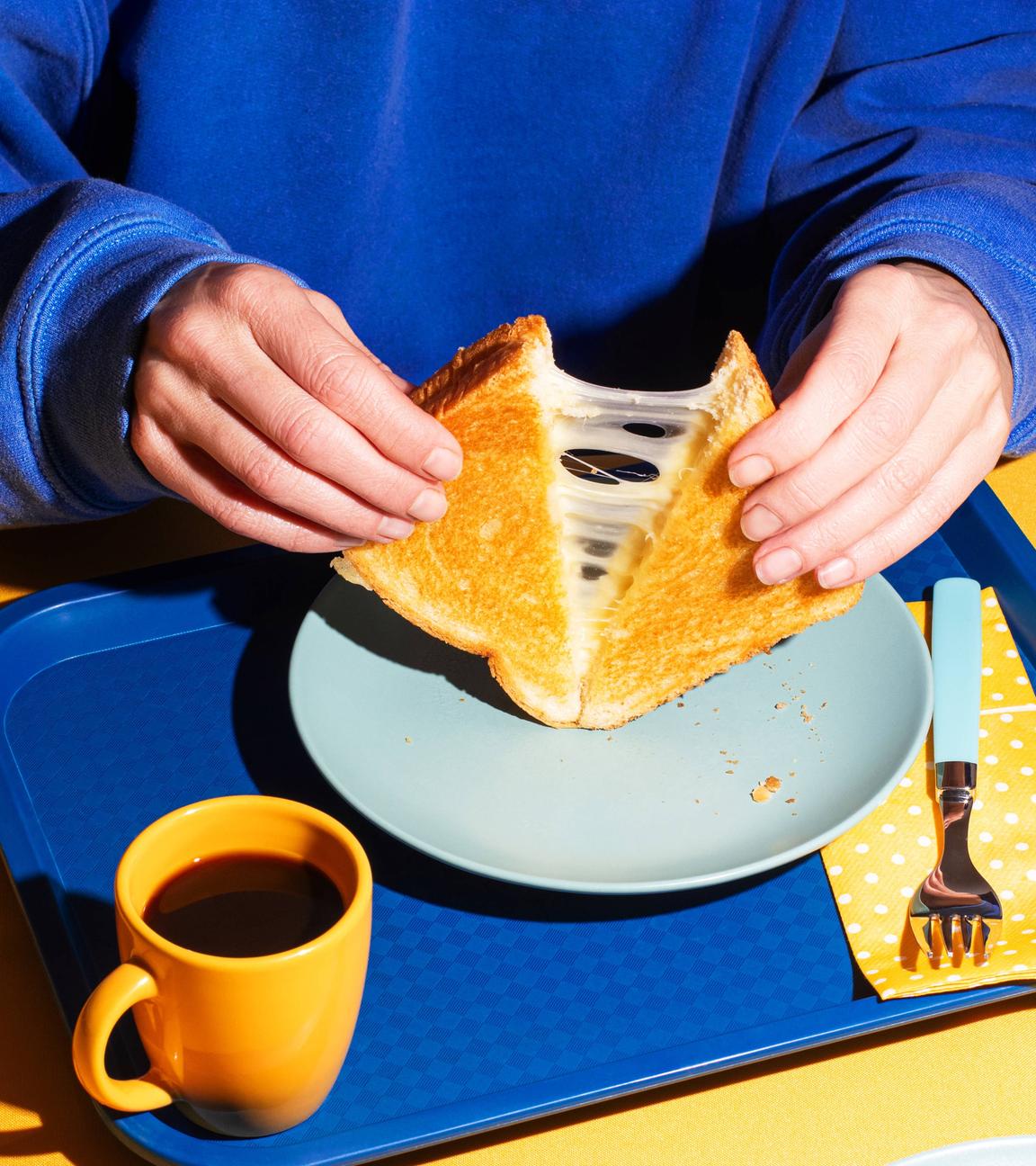 Eine Person zieht ein geschnittenes Sandwhich auseinander, das Käsefäden zieht.