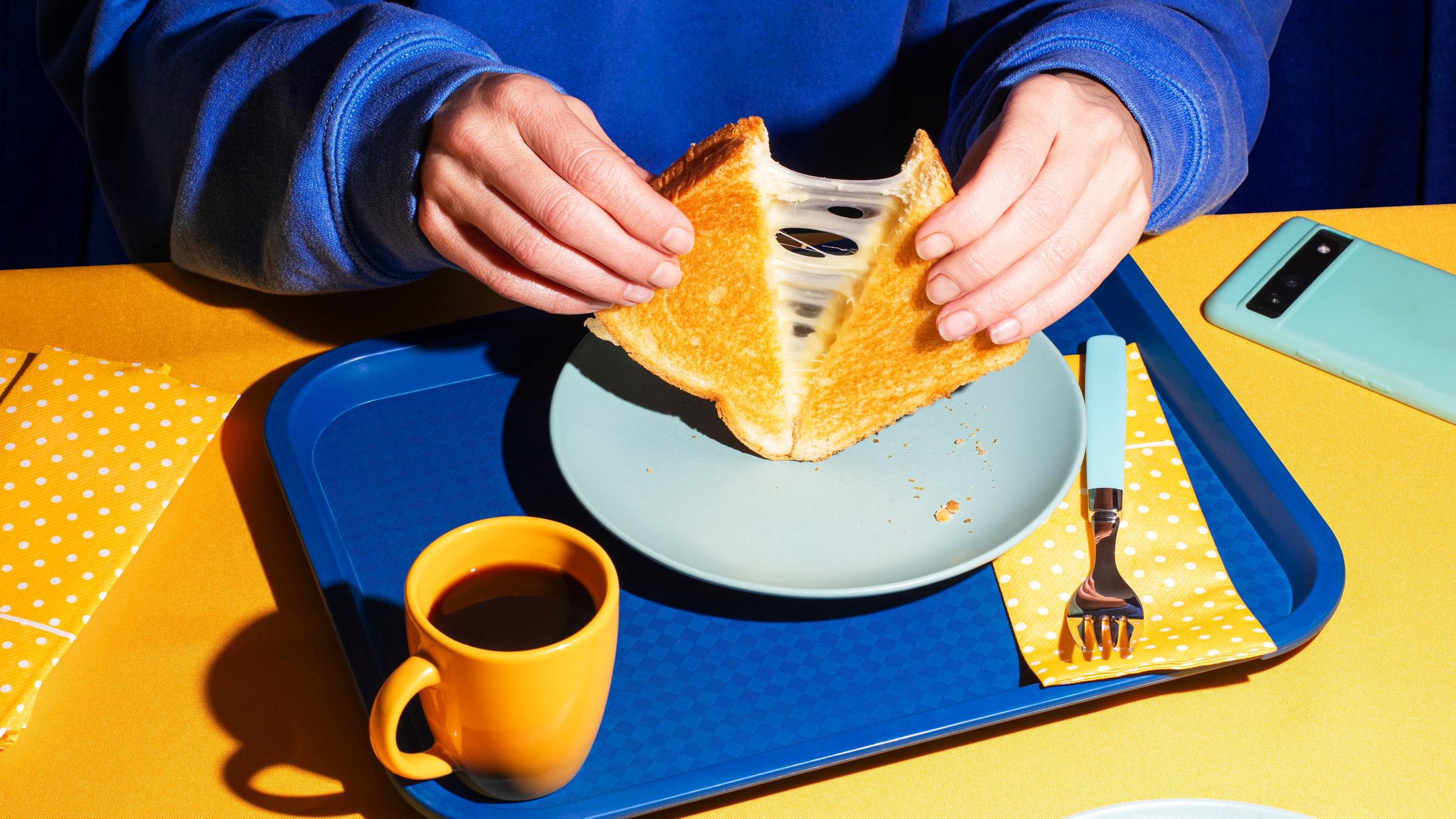 Eine Person zieht ein geschnittenes Sandwhich auseinander, das Käsefäden zieht.
