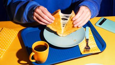 Eine Person zieht ein geschnittenes Sandwhich auseinander, das Käsefäden zieht.