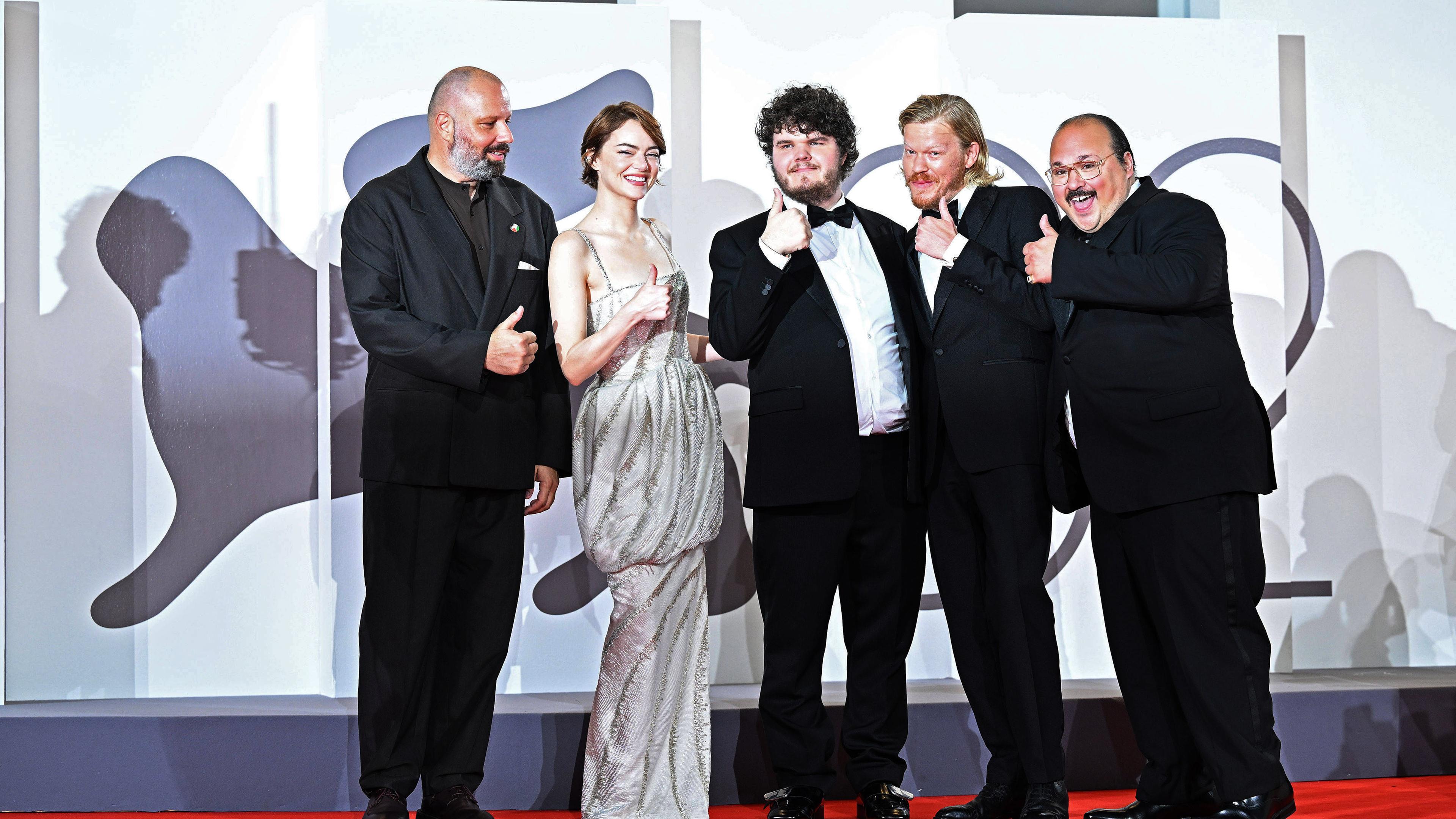 Gruppenfoto von vier Männern und einer Frau in Abendkleidung auf dem roten Teppich vor dem Logo der Filmfestspiele von Venedig.