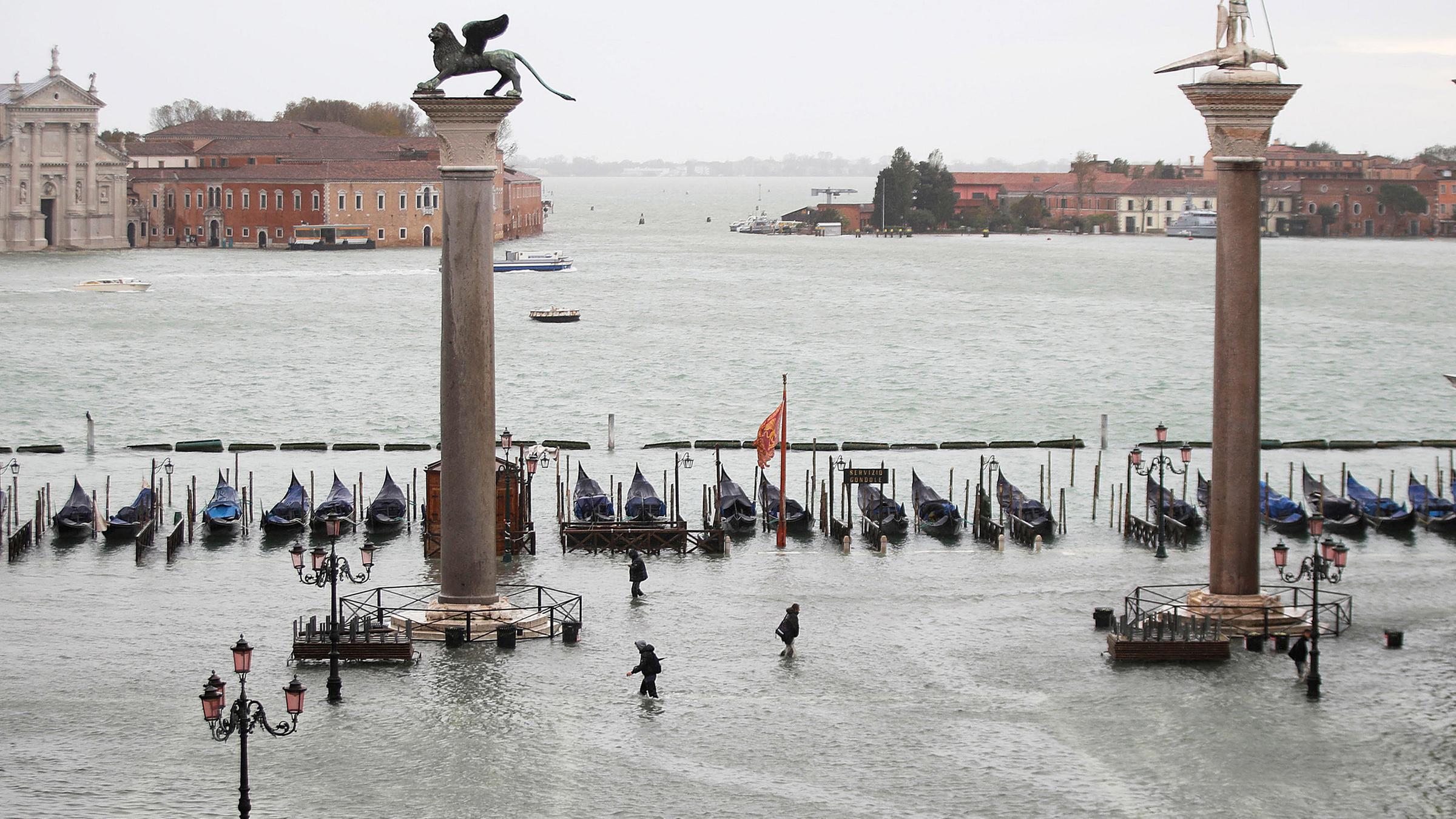 Menschen gehen knietief im Wasser über den überfluteten Markusplatz. Am 15.11.2019 in Venedig, Italien.