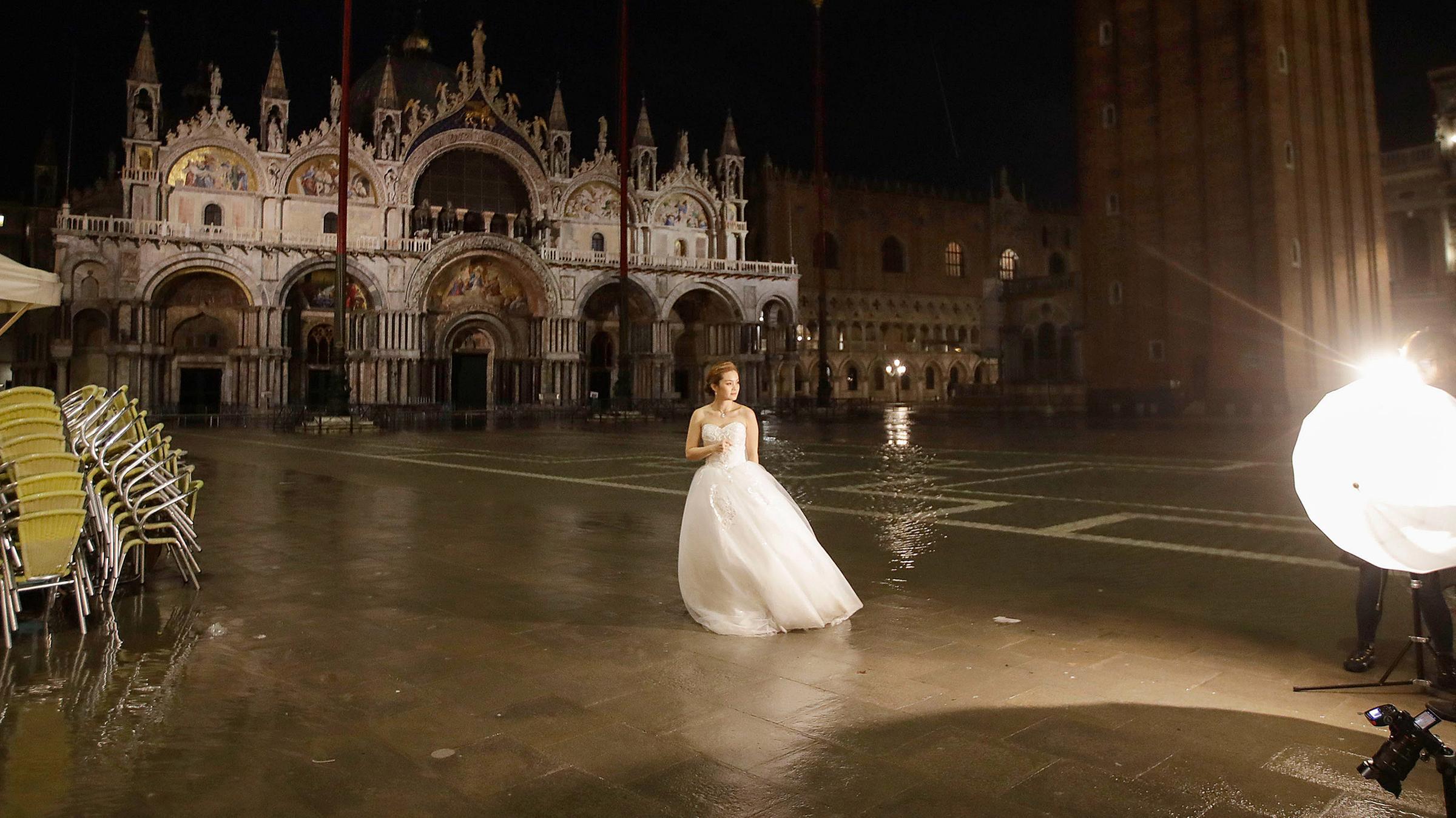 Eine Frau im Brautkleid steht am frühen Morgen auf dem überfluteten Markusplatz und wird fotografiert. Am 15.11.2019 in Venedig, Italien.