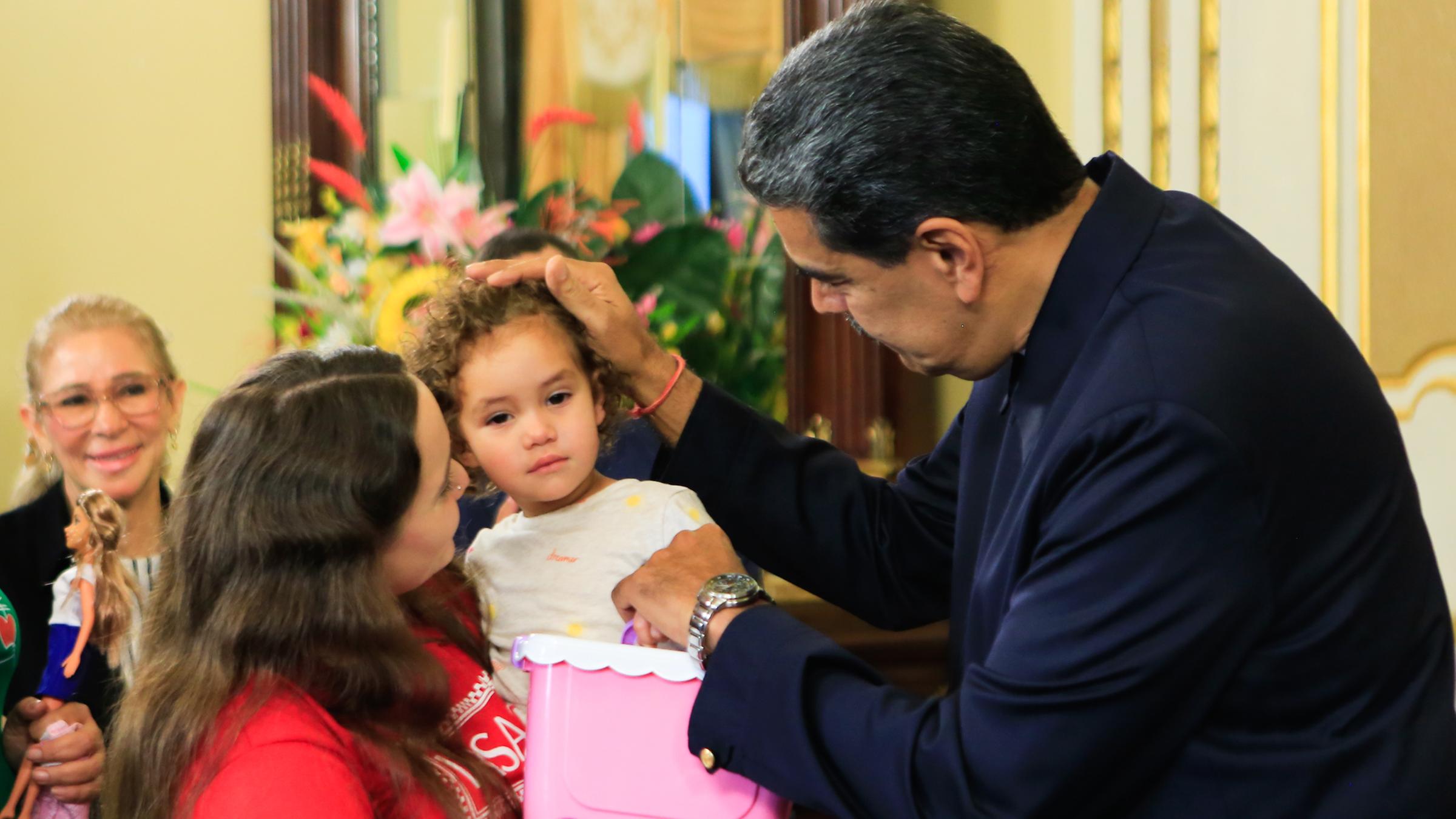 Yorely Bernal (l) trägt ihre Tochter Maikelys Espinoza (M) nach ihrer Ankunft in Venezuela auf dem Arm, während der venezolanische Präsident Nicolas Maduro das Kind streichelt.