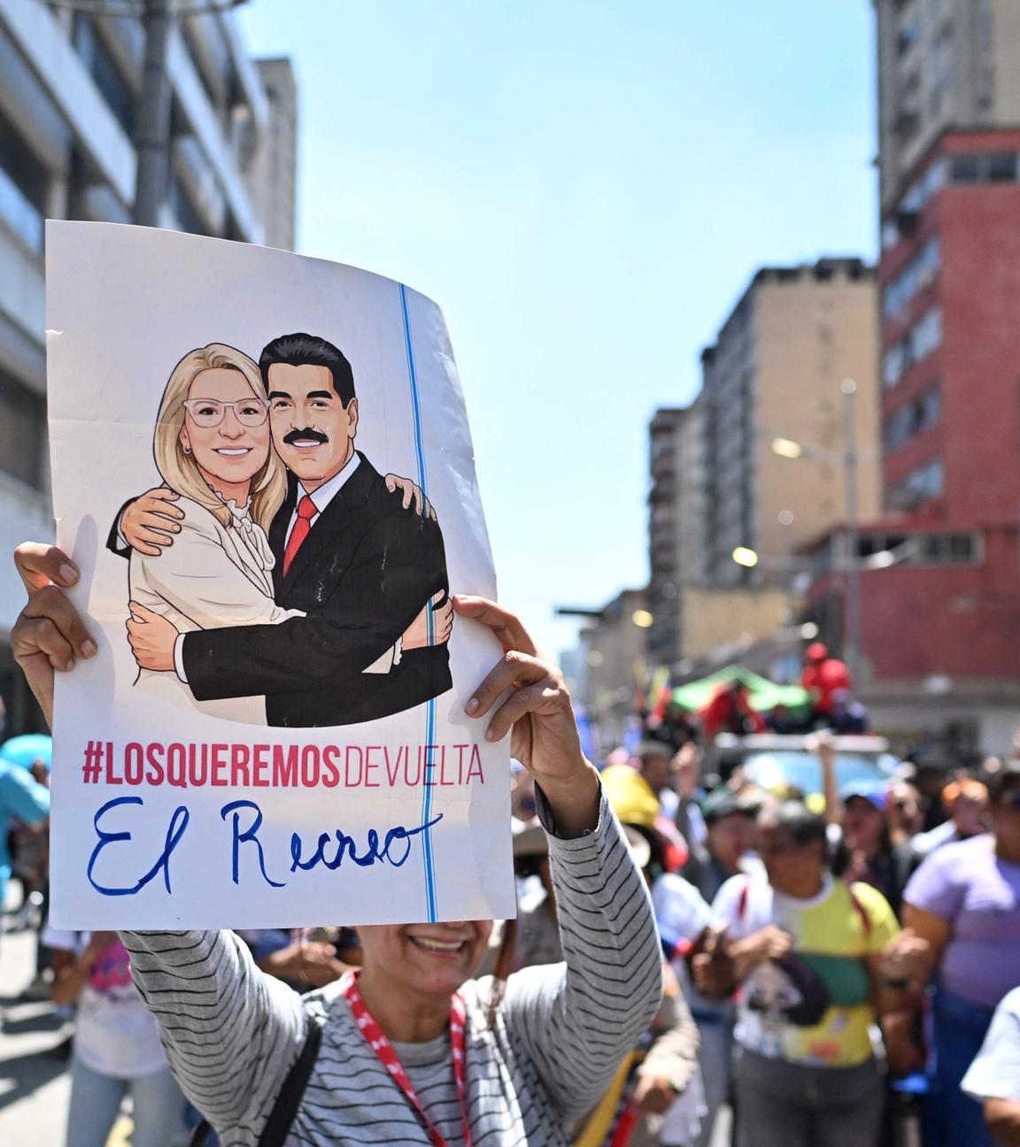 Gruppe von Protestierenden. Eine Person hält ein Plakat mit Darstellungen von Nicolás Maduro und seiner Frau Cilia Flores in die Kamera.