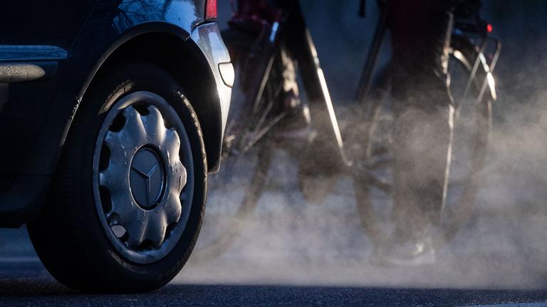 23.11.2021, Baden-Württemberg, Stuttgart: Ein Radfahrer steht neben einem Auto von Mercedes mit Dieselantrieb, dessen Abgase in der kalten Morgenluft sichtbar werden. 