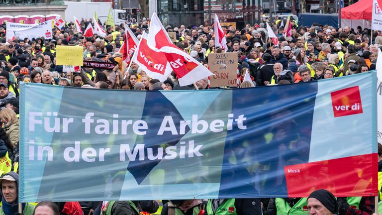 Ein Banner mit der Aufschrift "Für faire Arbeit in der Musik" ist bei einer Kundgebung von Verdi und der GEW auf dem Heumarkt zu sehen.