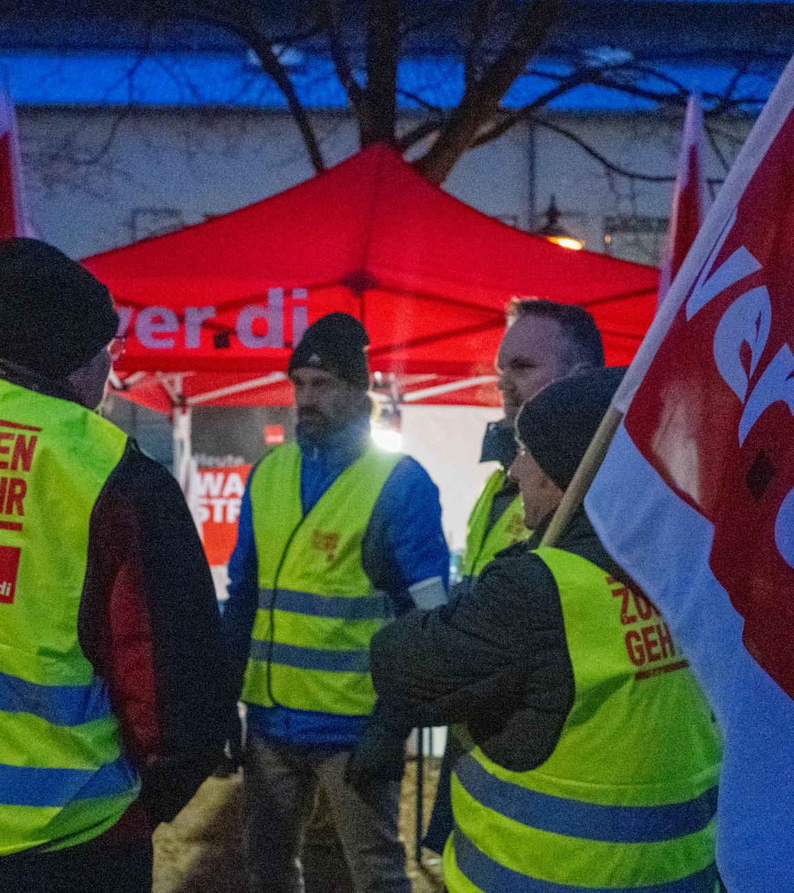 Streikende halten Fahnen der Gewerkschaft Verdi und sind mit Warnwesten gekleidet.
