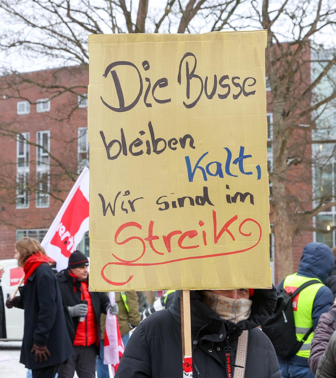 Eine Teilnehmerin hält bei einer Kundgebung in Hamburg-Harburg ein Schild mit der Aufschrift "Die Busse bleiben kalt, wir sind im Streik".