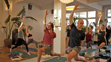 Gruppe an Personen in einem Studio, die Yoga betreiben.