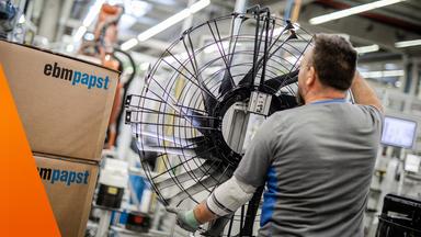 Arbeiter von hinten mit großem Ventilator-Rad in der Hand. Daneben Kartons von EBM-Papst