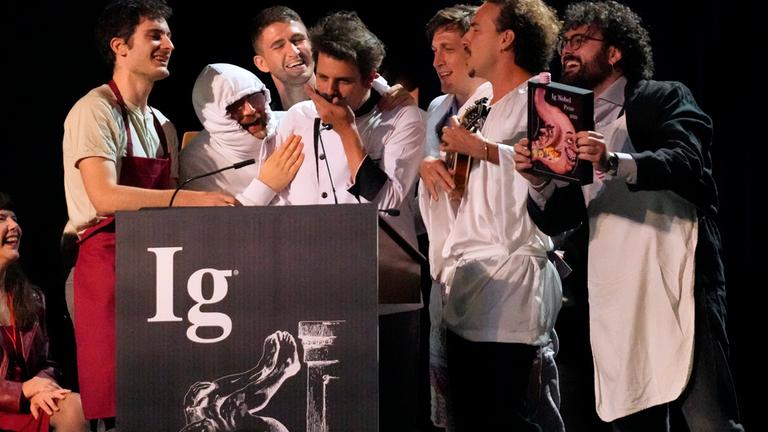 Der Ig-Nobelpreis für Ernährung wird von Daniele Dendi, Gabriel H. Segniagbeto, Roger Meek und Luca Luiselli entgegengenommen, die untersucht haben, inwieweit eine bestimmte Eidechsenart bestimmte Sorten von Pizza isst.