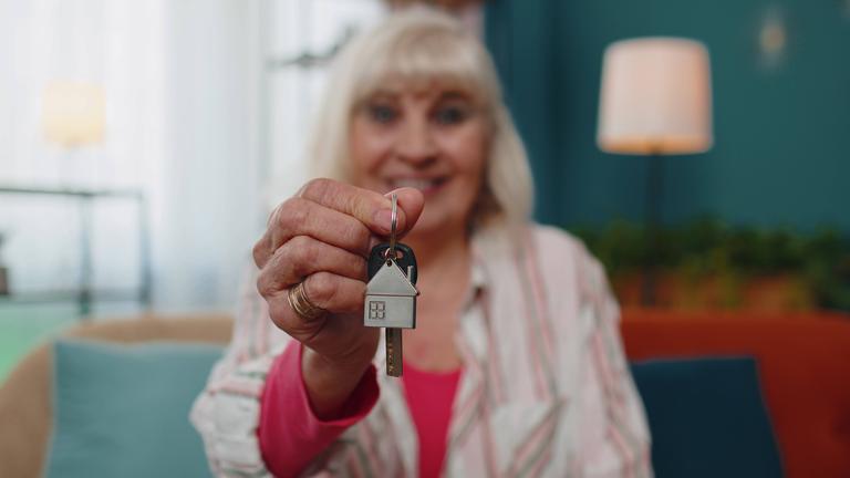 Eine ältere Frau hält lächelnd Wohnungsschlüssel einer Wohnung in die Kamera.