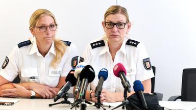 Zwei Polizeibeamtinnen sitzen bei einer Pressekonferenz an einem Tisch. Vor ihnen stehen mehrere Mikrofone verschiedener Medienvertreter.
