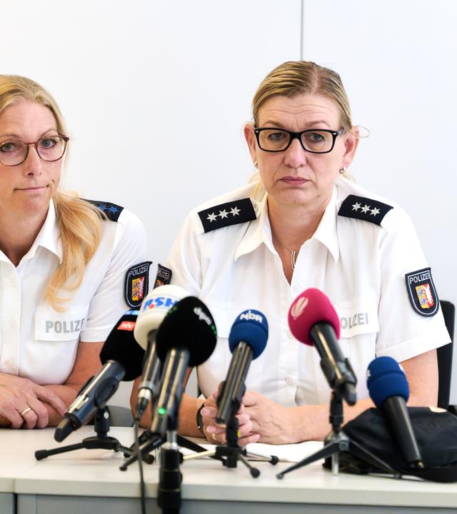 Zwei Polizeibeamtinnen sitzen bei einer Pressekonferenz an einem Tisch. Vor ihnen stehen mehrere Mikrofone verschiedener Medienvertreter.