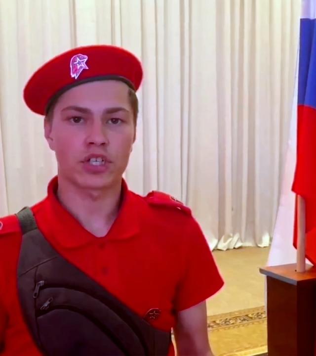 Denis in russischer Uniform  neben einer russoschen Flagge 