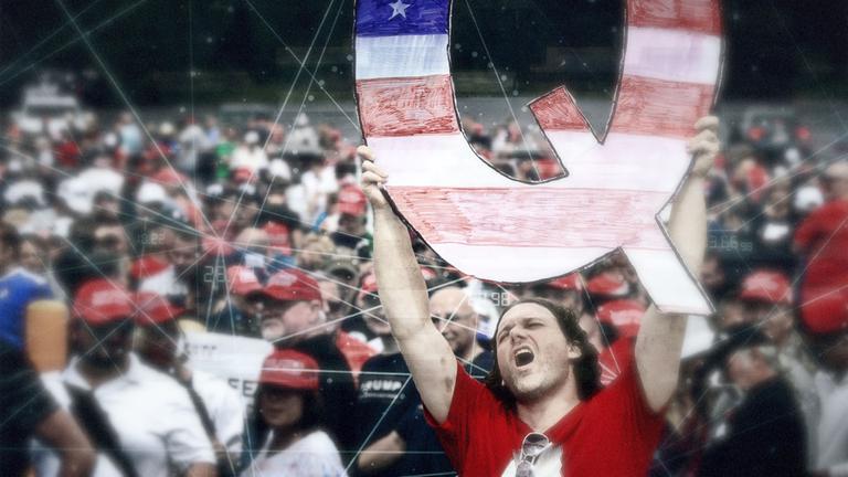 Man in der Menge hebt ein großes Q in die Höhe.