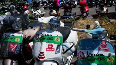 Drei unterschiedliche Vespa-Roller stehen zusammen mit vielen anderen Rollern in Rom. Die Vespas sind geschmückt für den 80. Geburtstag der Vespa.