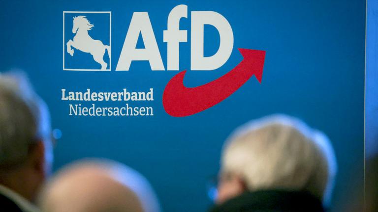 Delegierte sitzen bei der Aufstellungsversammlung der AfD Niedersachsen vor dem Partei-Logo.