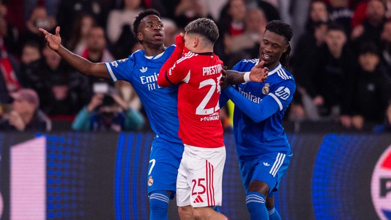 Gianluca Prestianni (Benfica Lissabon, Mitte) hält sich das Trikot vor den Mund, Vinicius Junior (Real Madrid, links) breitet die Arme aus.