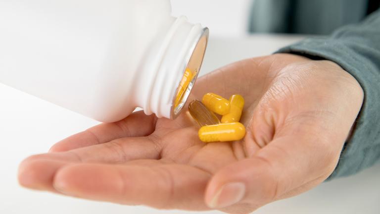Eine Frau gibt Nahrungsergänzungsmittel in Form von Kapseln auf ihre Hand.