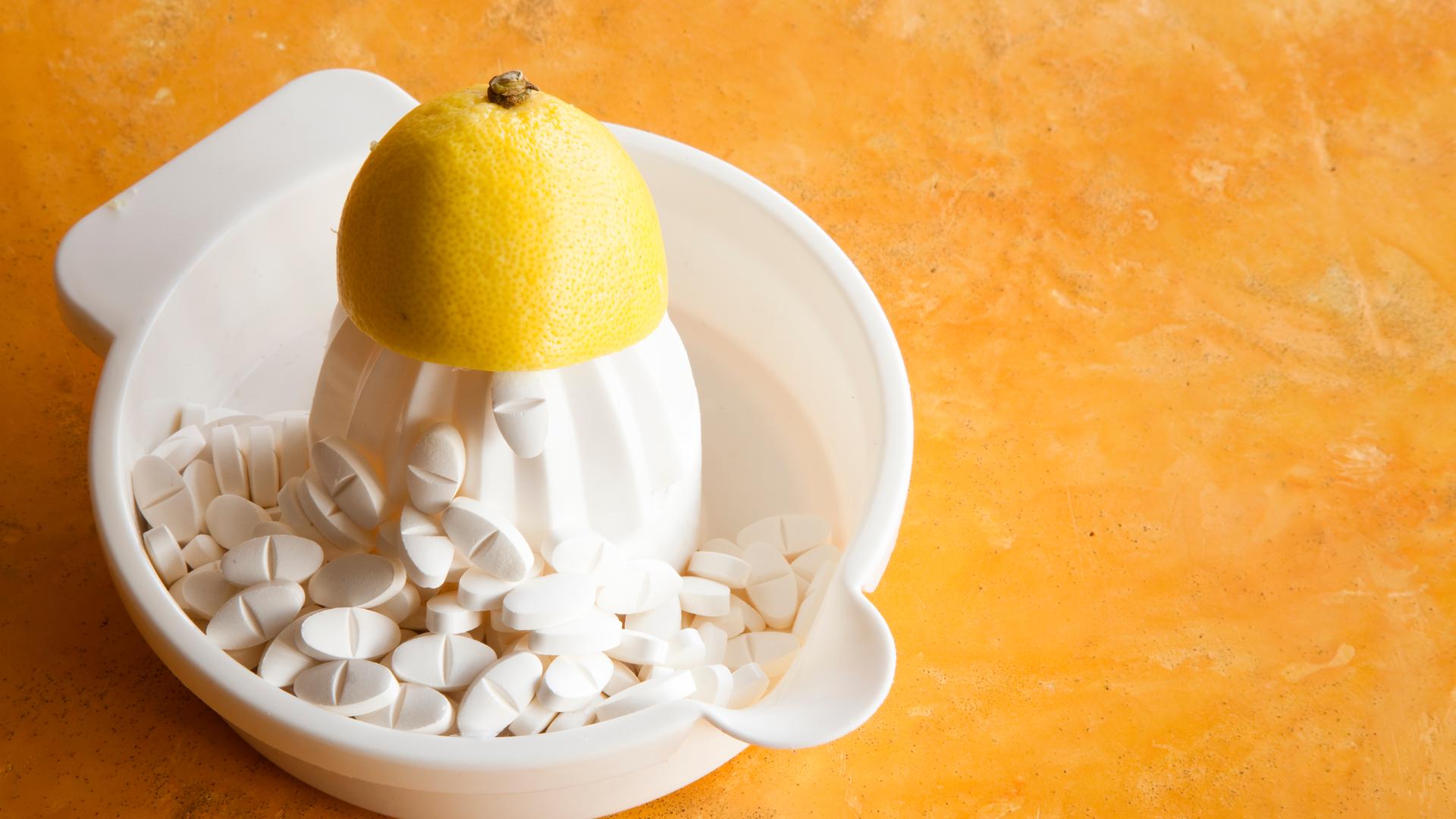 Eine Zitrone liegt auf einer Zitronenpresse, daneben sind Tabletten zu sehen. Symbolfoto.