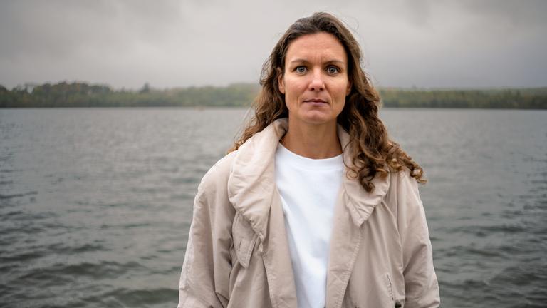 Frau mit braunen, langem lockigem Haar schaut in die Kamera.