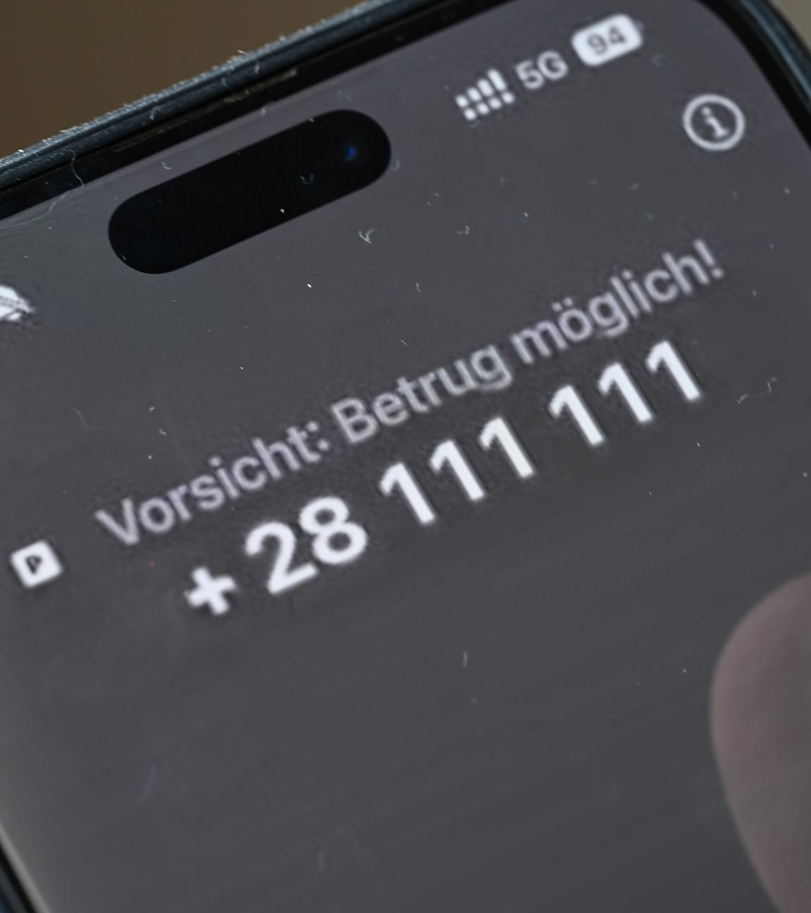 Ein Mann hält ein Smartphone, auf dem der Warntext "Vorsicht: Betrug möglich!" zu lesen ist.