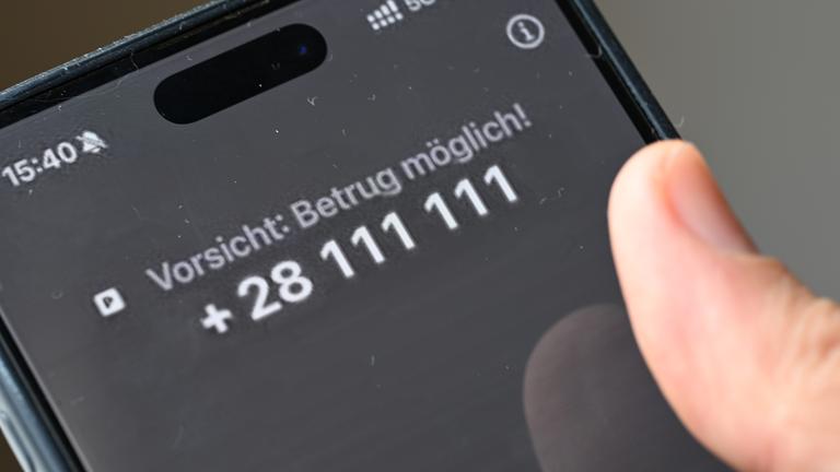 Ein Mann hält ein Smartphone, auf dem der Warntext "Vorsicht: Betrug möglich!" zu lesen ist.