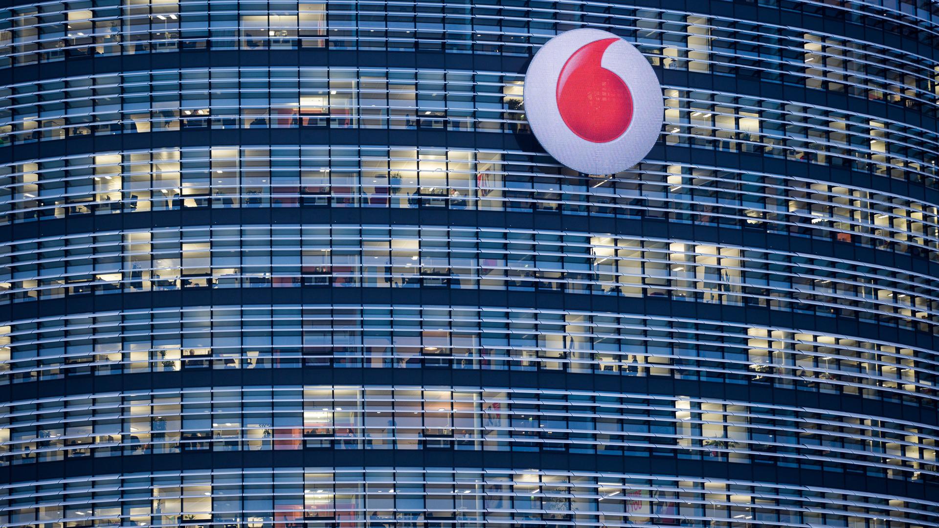 Man sieht ein Hochhaus in der Dämmerung mit vielen Fenstern und dem Vodafone Logo davor.