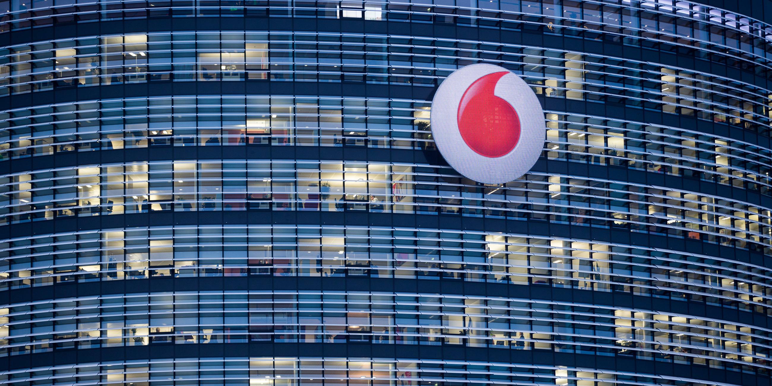 Man sieht ein Hochhaus in der Dämmerung mit vielen Fenstern und dem Vodafone Logo davor.
