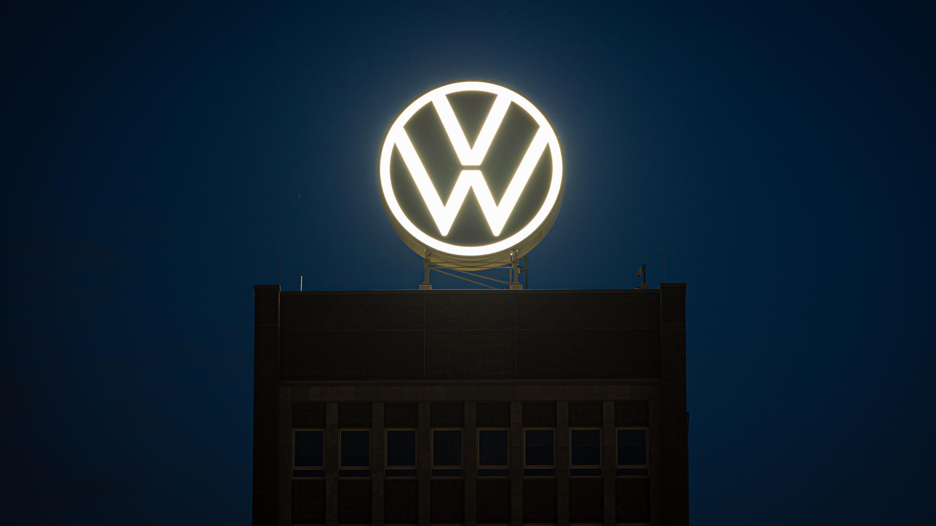 Das VW-Logo leuchtet auf dem Dach des Markenhochhauses im Volkswagen Stammwerk am frühen Morgen.