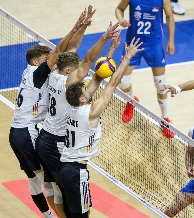 In der Volleyballpartie spielt das serbische Nationalteam den Ball über das Netz und zwingt damit das deutsche Nationalteam zur Abwehr