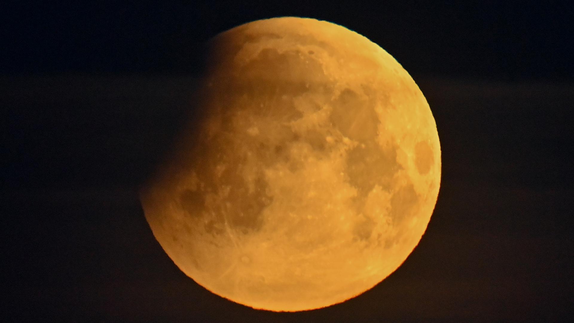 Ein orange gefärbter Mond tritt langsam in den Erdschatten: Beginn einer Mondfinsternis