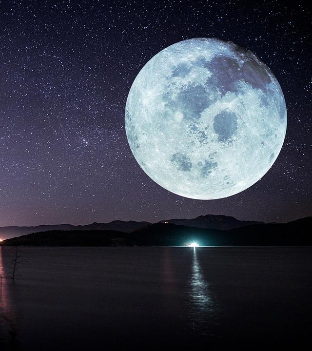 Eine Meeresküste bei einer Vollmondnacht. Der Himmel ist voller Sterne, im Hintergrund sieht man Berge. Der Mond ist riesig und sehr deutlich zu sehen.