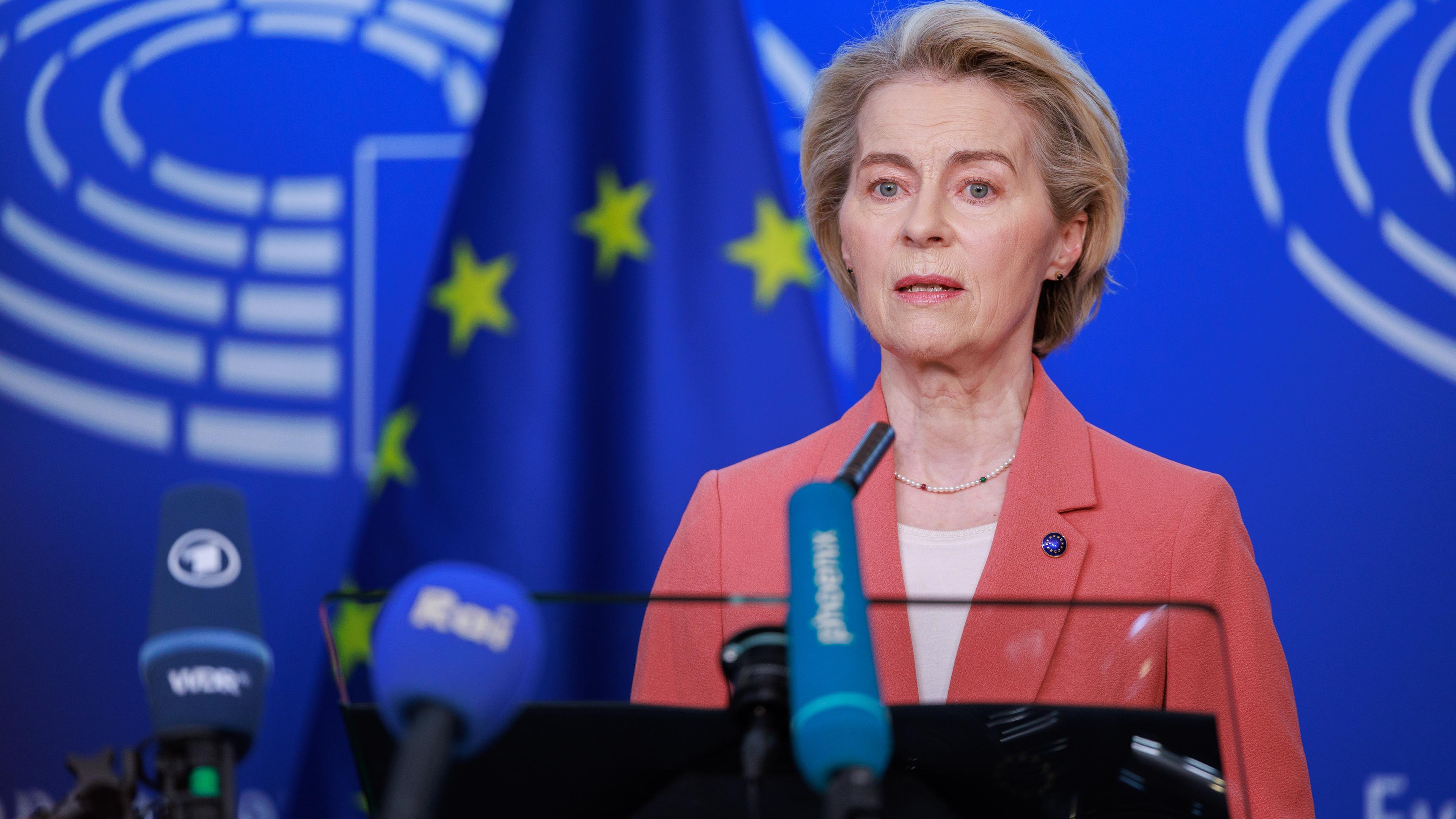Ursula von der Leyen spricht vor einer blauen Wand. Vor ihr stehen Mirkofone.