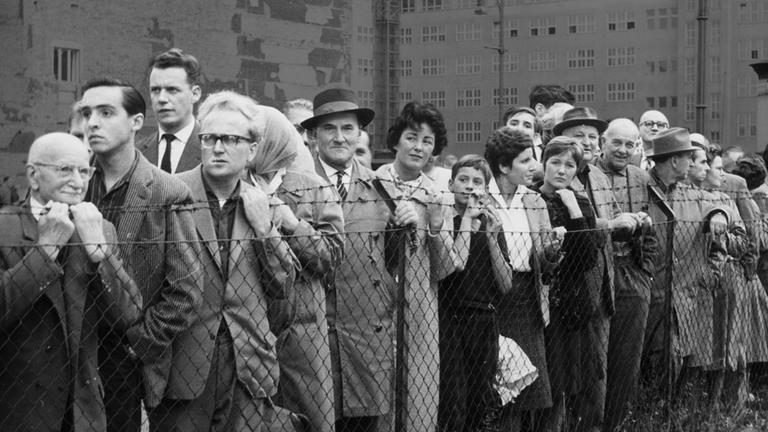 Viele Menschen stehen an einem Stacheldrahtzaun.