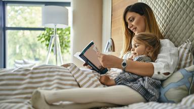 Mutter und Tochter lesen ein Buch im Bett (Symbolfoto)