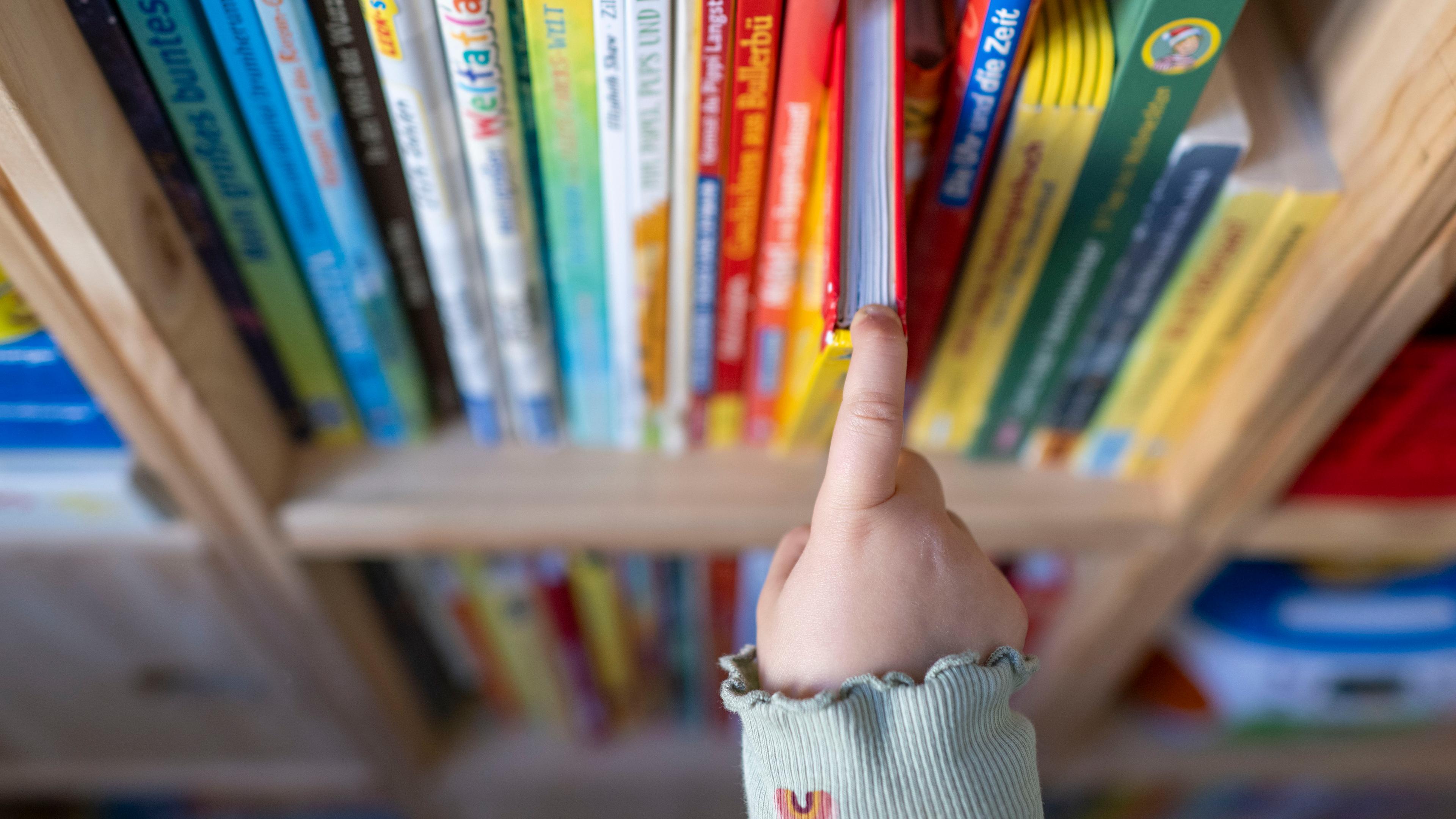 Sachsen, Leipzig: Ein Mädchen zieht in einem Kinderzimmer in Leipzig ein Kinderbuch aus einem Regal.