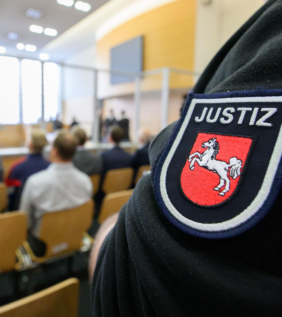 Ausschnitt aus dem Gerichtssaal. Es sind einige Besucher anwesend. Außerdem ist Personal der Justiz zu sehen.