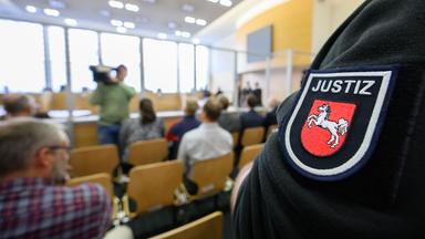 Ausschnitt aus dem Gerichtssaal. Es sind einige Besucher anwesend. Außerdem ist Personal der Justiz zu sehen.