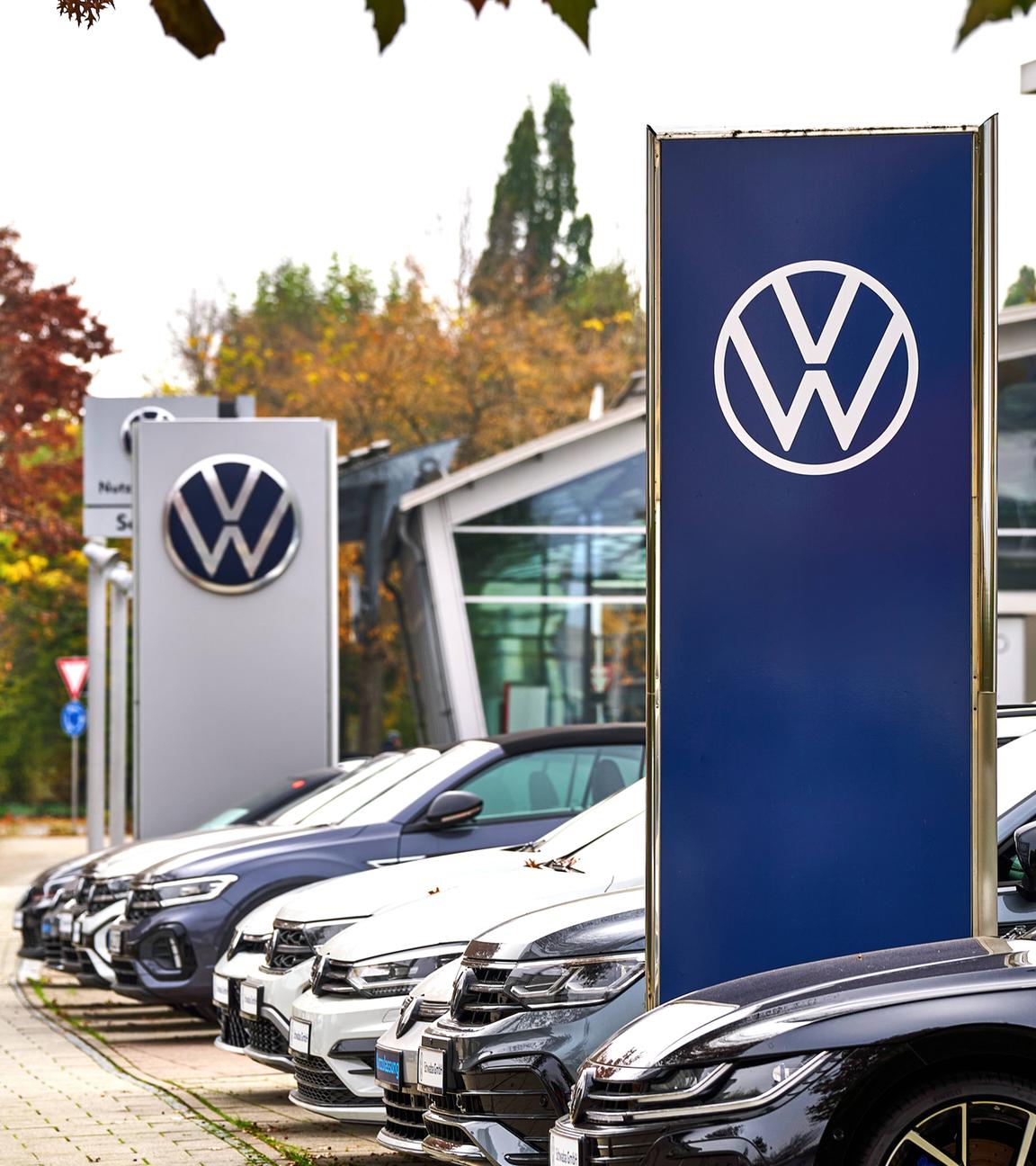 Parkplatz eines VW-Autohändlers mit zahlreichen Neuwagen und VW-Schild.
