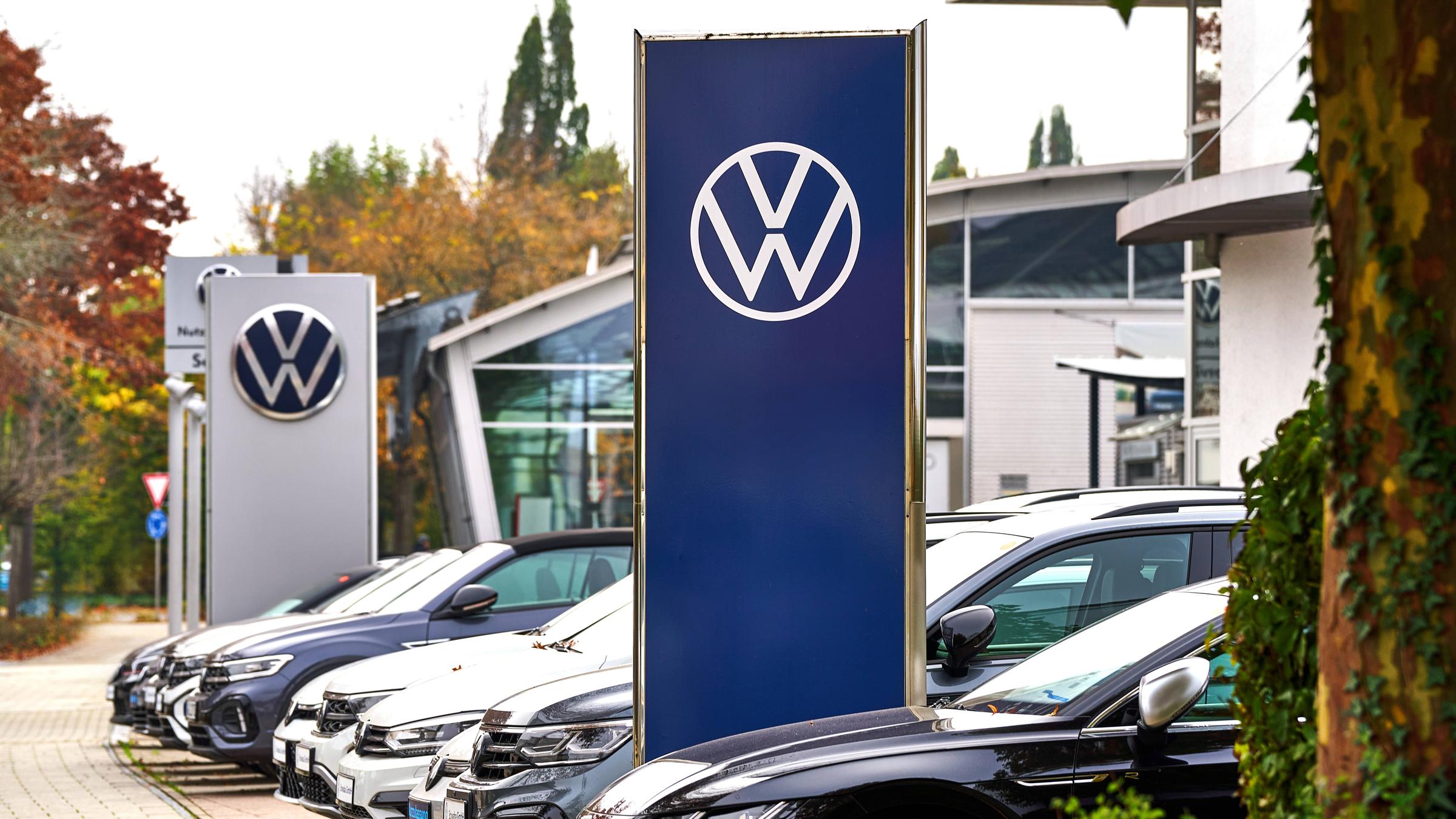Parkplatz eines VW-Autohändlers mit zahlreichen Neuwagen und VW-Schild.