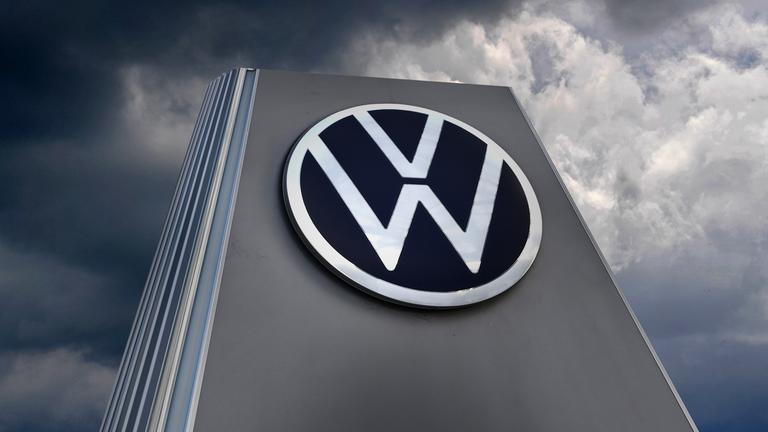 VW-Schild vor dunklen Wolken.
