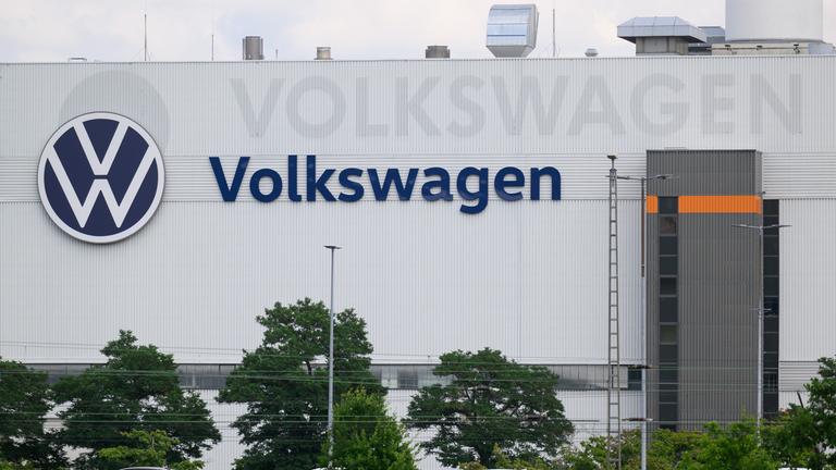 Eine graue Fabrikhalle, auf deren Wand in blau "Volkswagen" steht, daneben das VW-Logo.