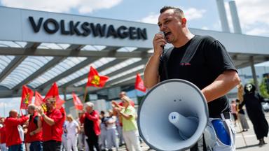 Mann mit Megafon vor einem VW-Werk, vor dem ein Protest der IG-Metall stattfindet.