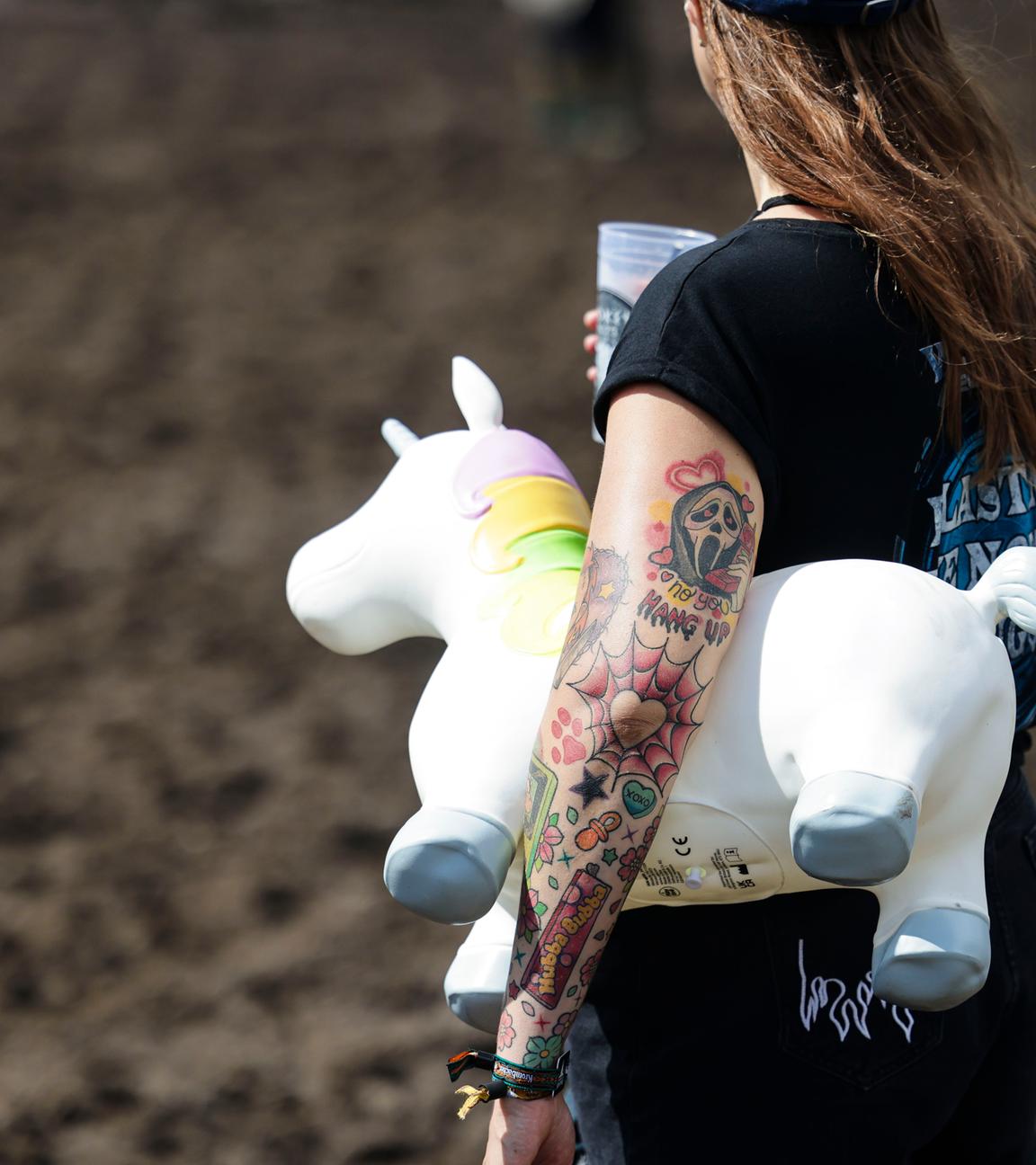 Eine Frau hält ein Plastikeinhorn unter dem Arm vor der Bühne beim Wacken Open Air.