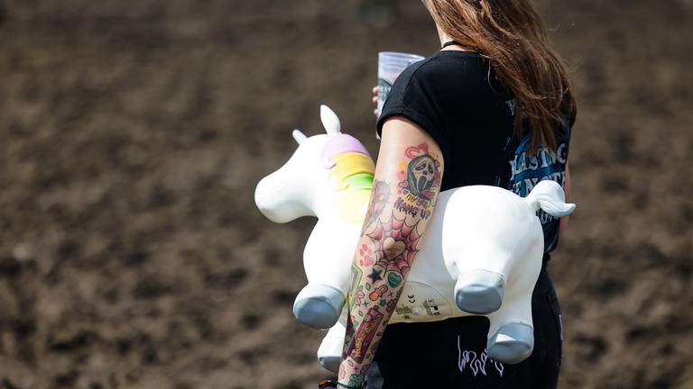 Eine Frau hält ein Plastikeinhorn unter dem Arm vor der Bühne beim Wacken Open Air.