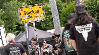 Schleswig-Holstein, Wacken: Teilnehmer des Wacken Open Air (WOA) fotografieren sich vor dem Ortseingangsschild von Wacken.