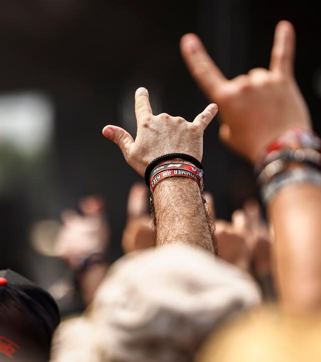 Fans beim Wacken Open Air recken die Hände mit gestrecktem Zeigefinger und kleinem Finger hoch zum Metal-Gruß.